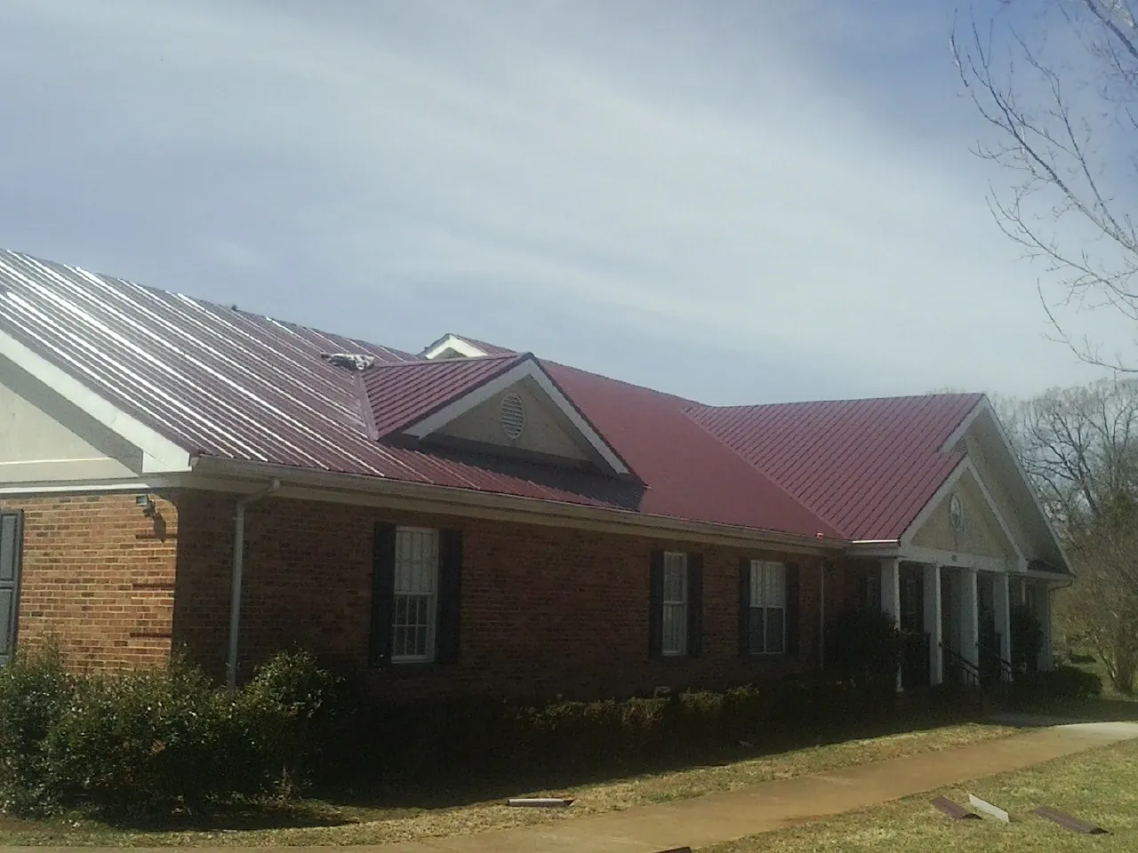 Red metal roof with gabled entries on a long brick building, from a Hail Damage Roof Repair job in Ashford